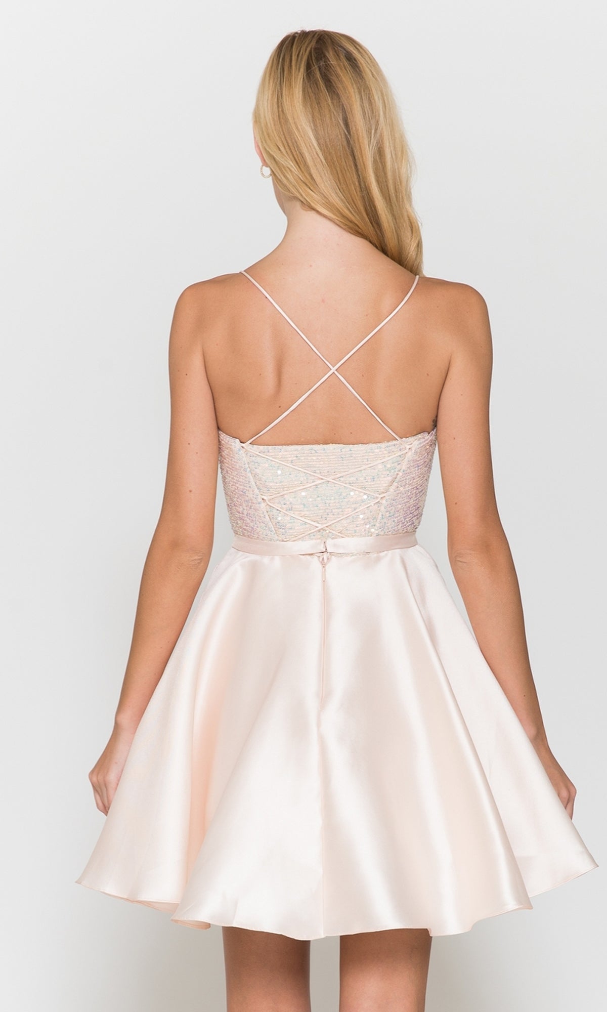 A woman with long blonde hair is shown from the back wearing the Sequin-Bodice Short Flared Homecoming Dress 8730, featuring a light pink a-line silhouette with crisscross spaghetti straps and a flared skirt.